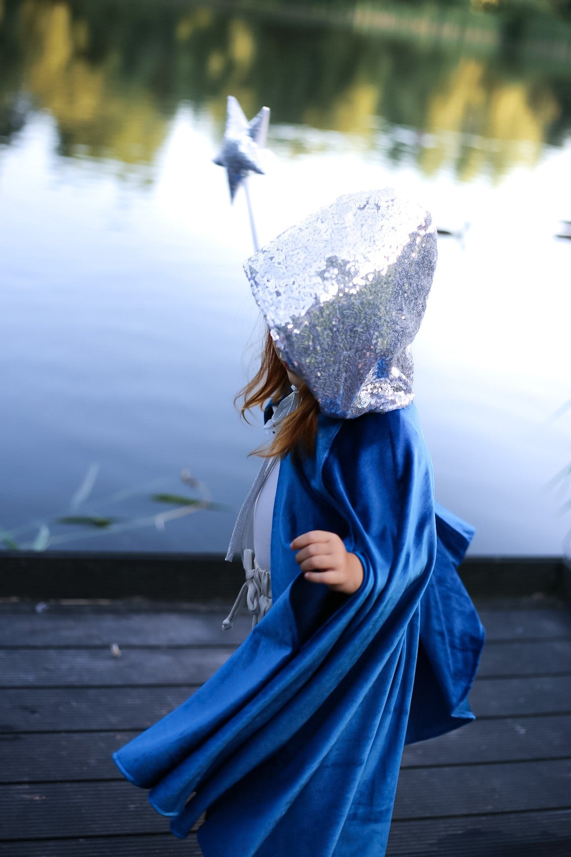 A young girl in a flowing Snow Queen Magic Cape by Moi Mili catching the wind in a sunny natural landscape