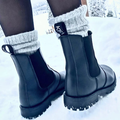 Black rubber boots with thick soles worn in the snow, paired with gray socks.