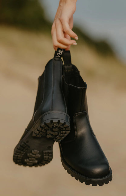 Black boots held by a hand against a blurred natural background