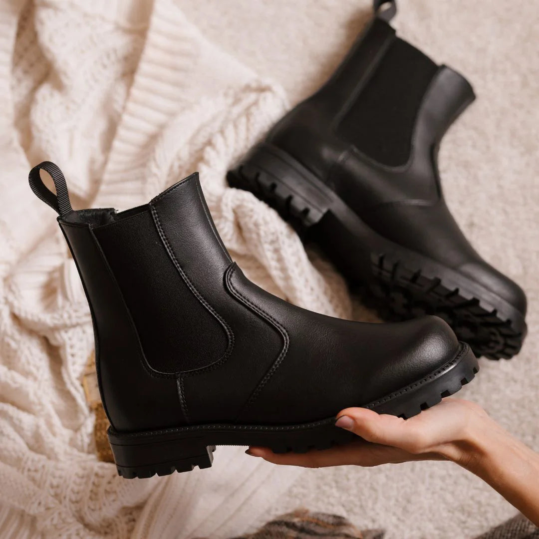 Black rubber boots being held against a textured beige background