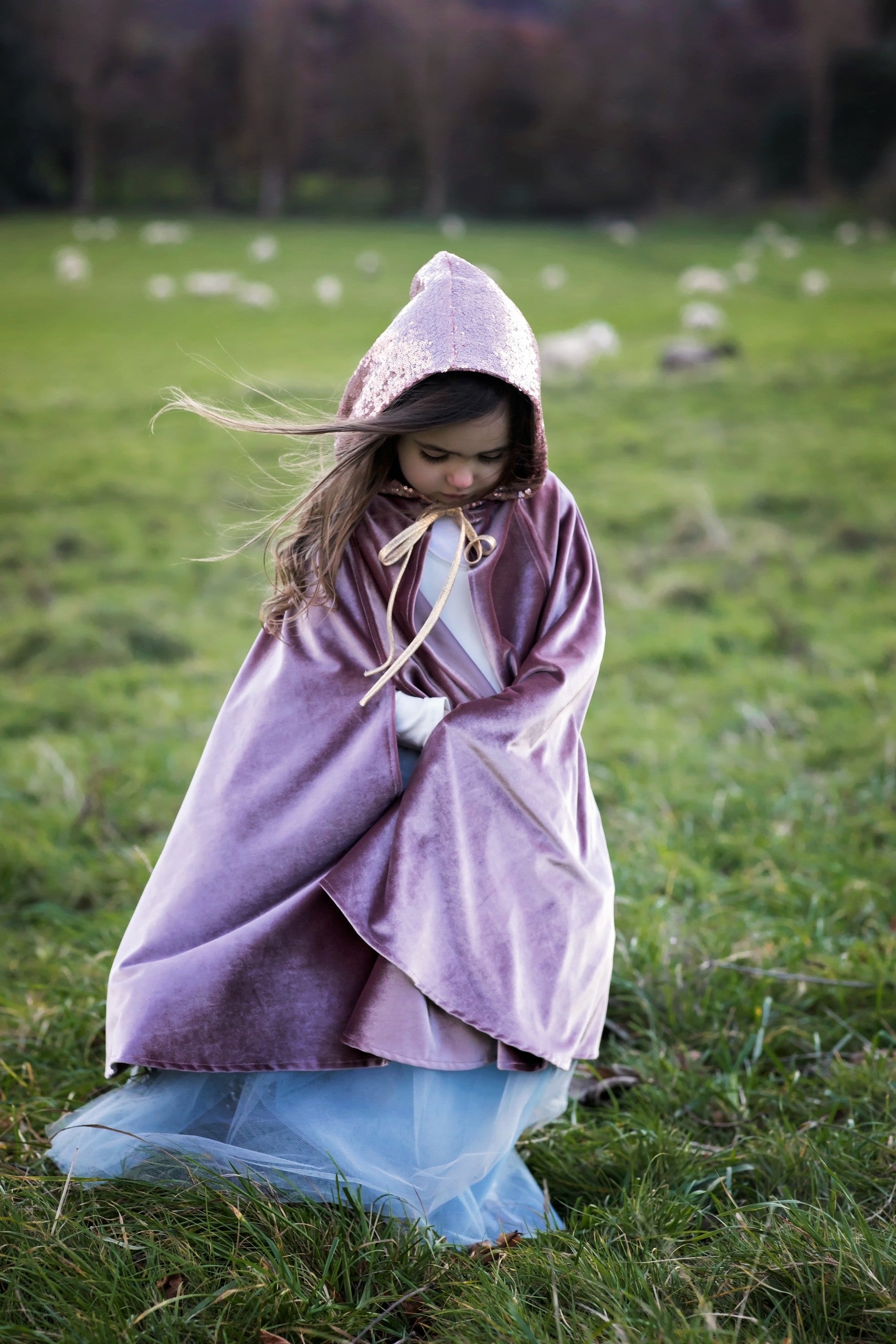 A young girl in a flowing Magic Cape Cosmic Pearl by Moi Mili catching the wind in a sunny natural landscape