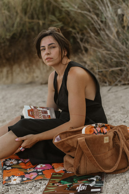 Moi Mili Mom Weekender Bag Caramel: a mother resting on the grass while reading a book in natural surroundings