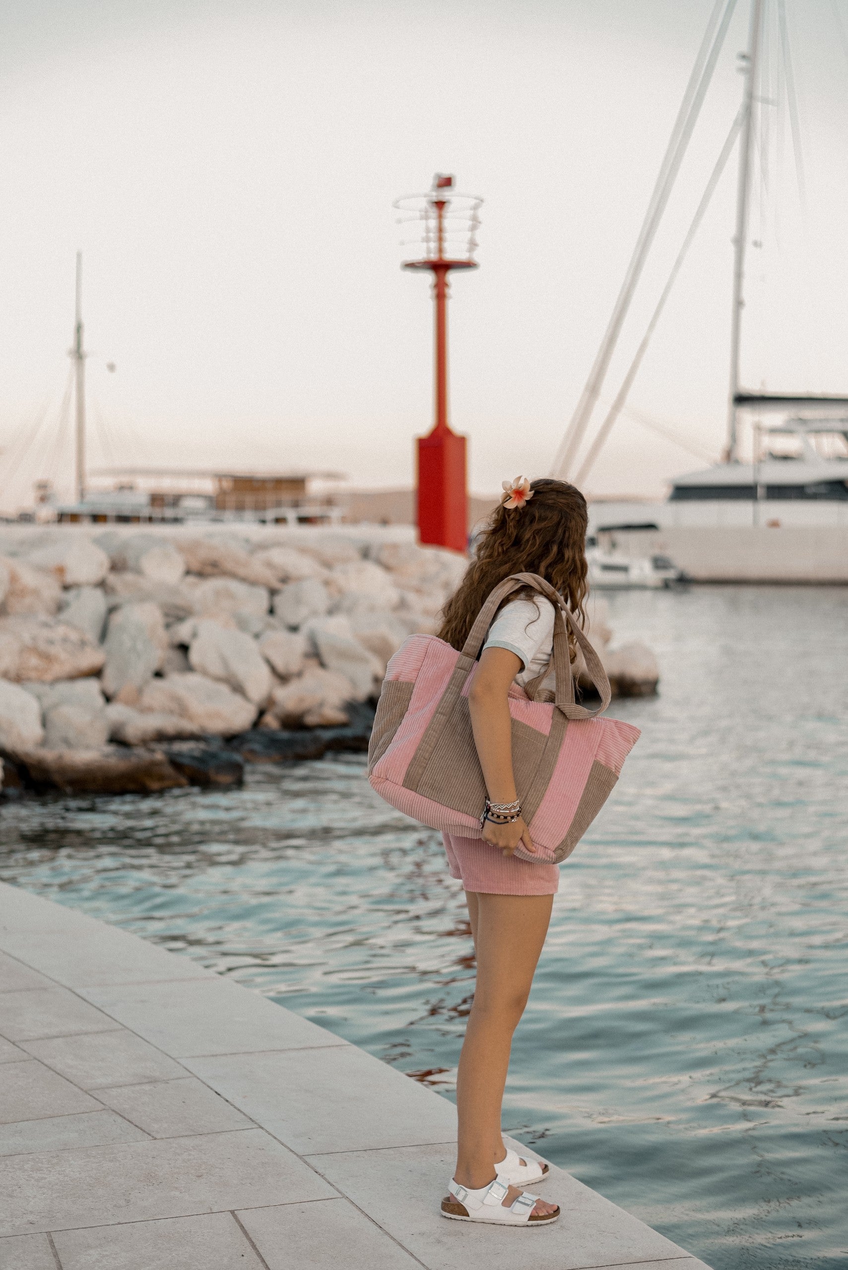 Moi Mili Mom Weekender Bag Pink Coffee: a young woman walking along a wooden dock carrying a large quilted cotton travel bag
