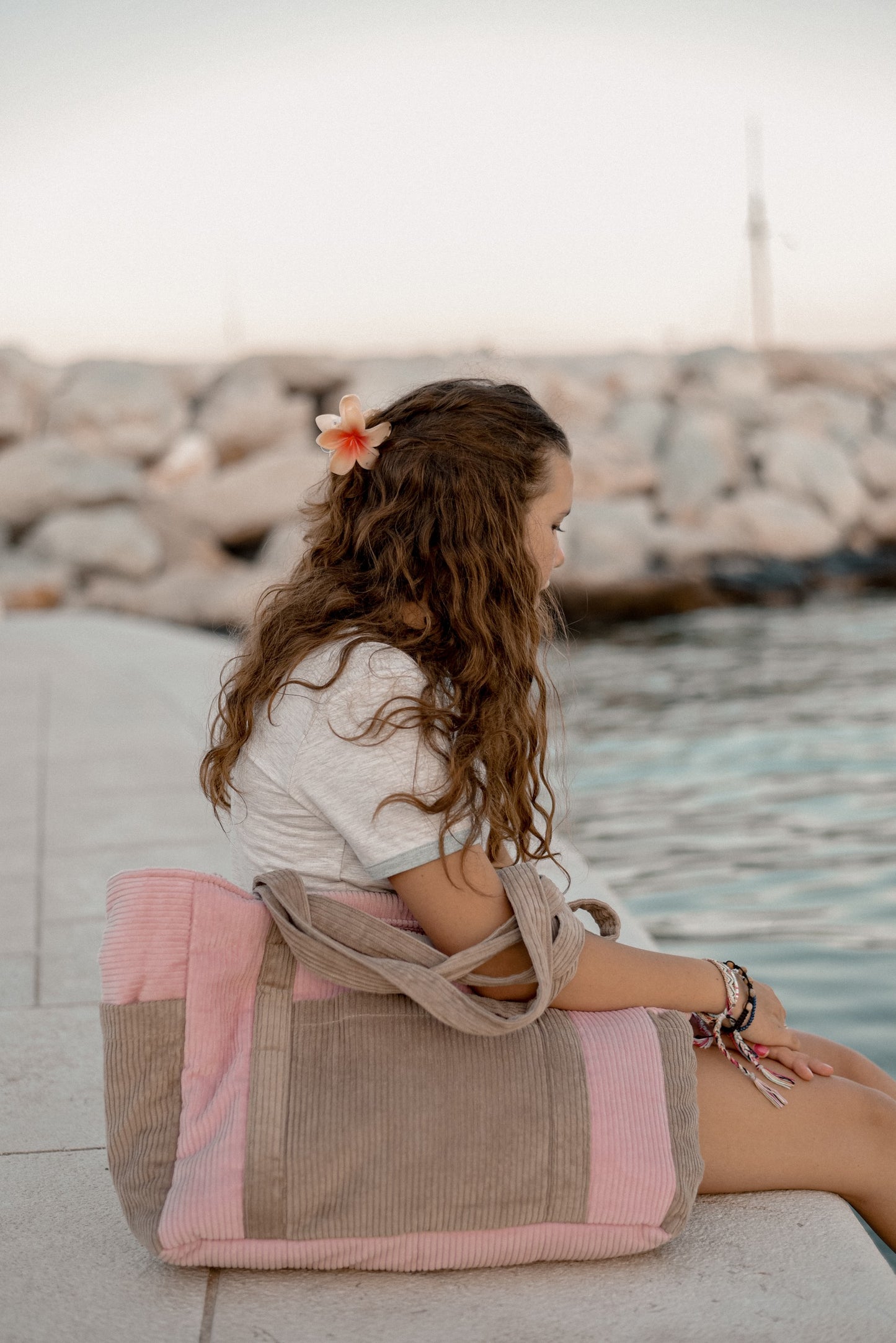 Moi Mili Mom Weekender Bag Pink Coffee: a young woman resting on dock with her large quilted cotton bag beside her at the waterfront
