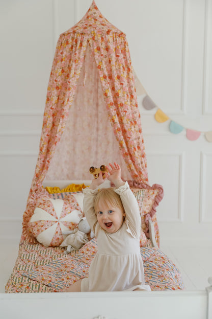 Spring Garden nursery: a joyful child playing with toys on a bed under a vibrant floral Organic Cotton Canopy