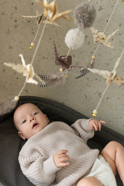 Sensory playtime: a curious baby reaching for the hanging shapes of a Moi Mili Gold Dust Origami Nursery Mobile in a bright room