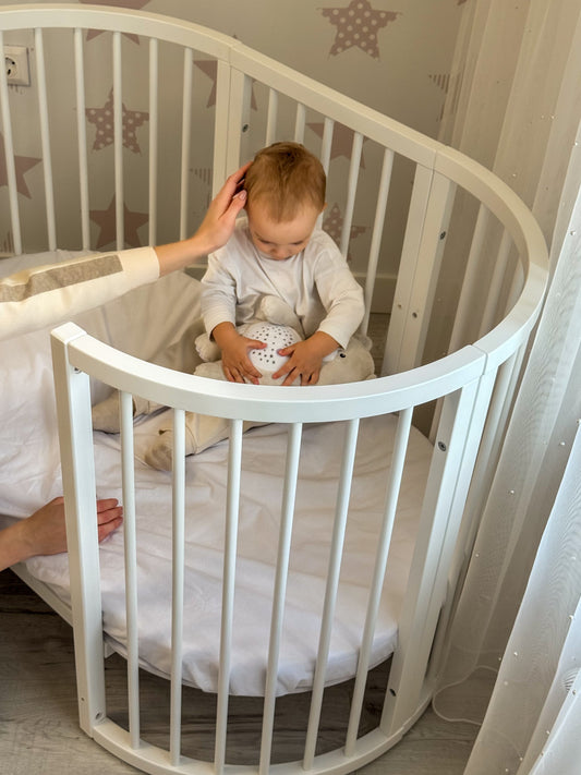 baby  sitting inside the Round Baby Crib OLIN with Mattress - White playing with a soft toy