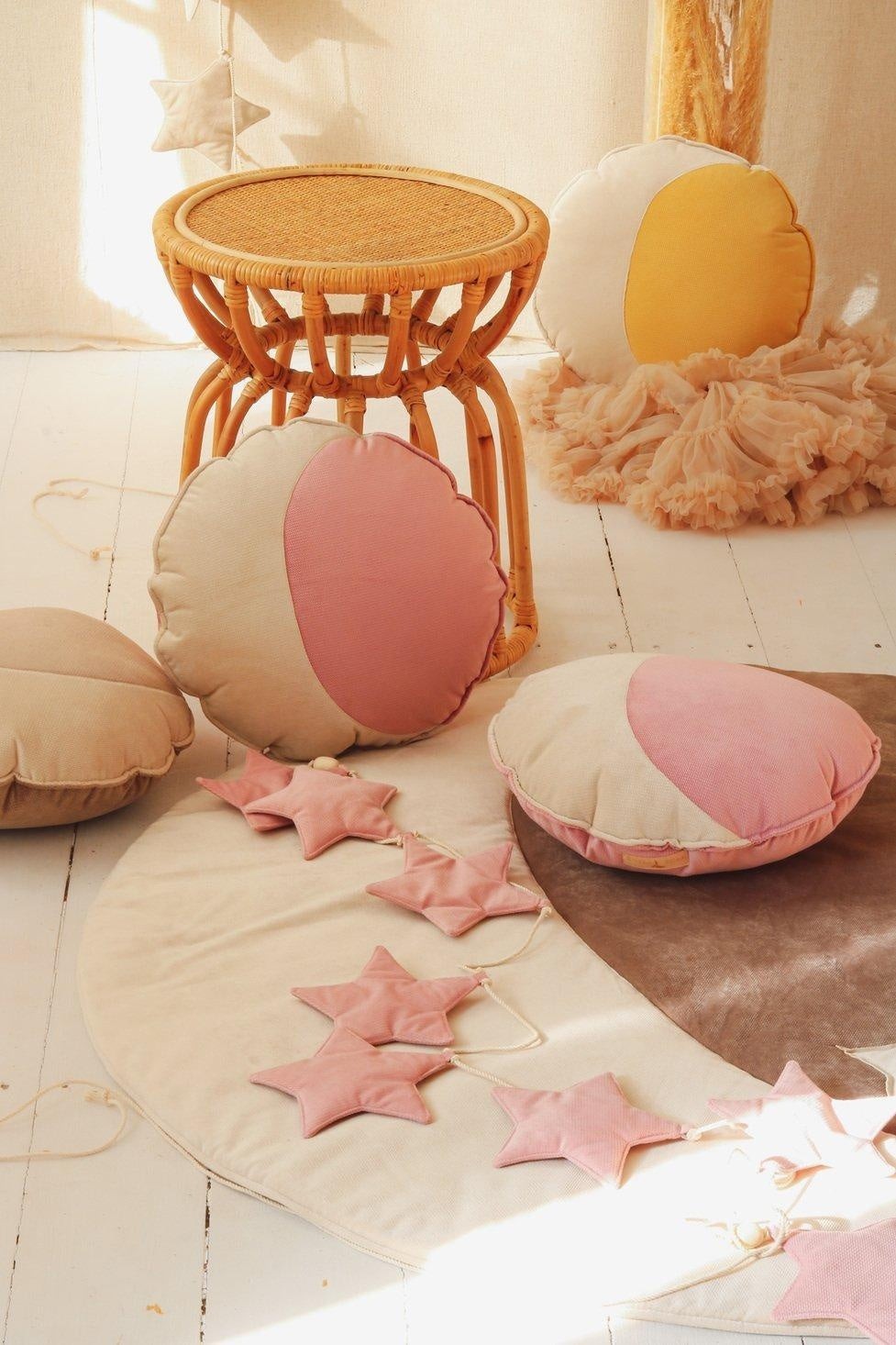 Scandi nursery decor: a Moi Mili Soft Pink Dust Star Garland resting on a woven cotton playmat over a beautiful natural wood floor in a cozy room corner