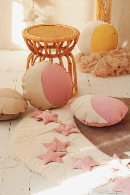 Scandi nursery decor: a Moi Mili Soft Pink Dust Star Garland resting on a woven cotton playmat over a beautiful natural wood floor in a cozy room corner