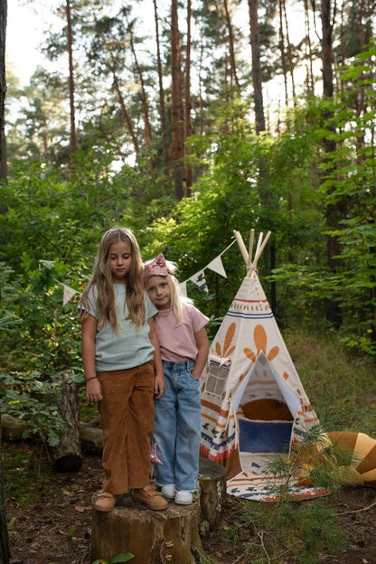 Wild and free kids: two children playing near a Moi Mili Native Vibe Teepee Tent set up in a beautiful pine forest, creating a magical woodland hideout