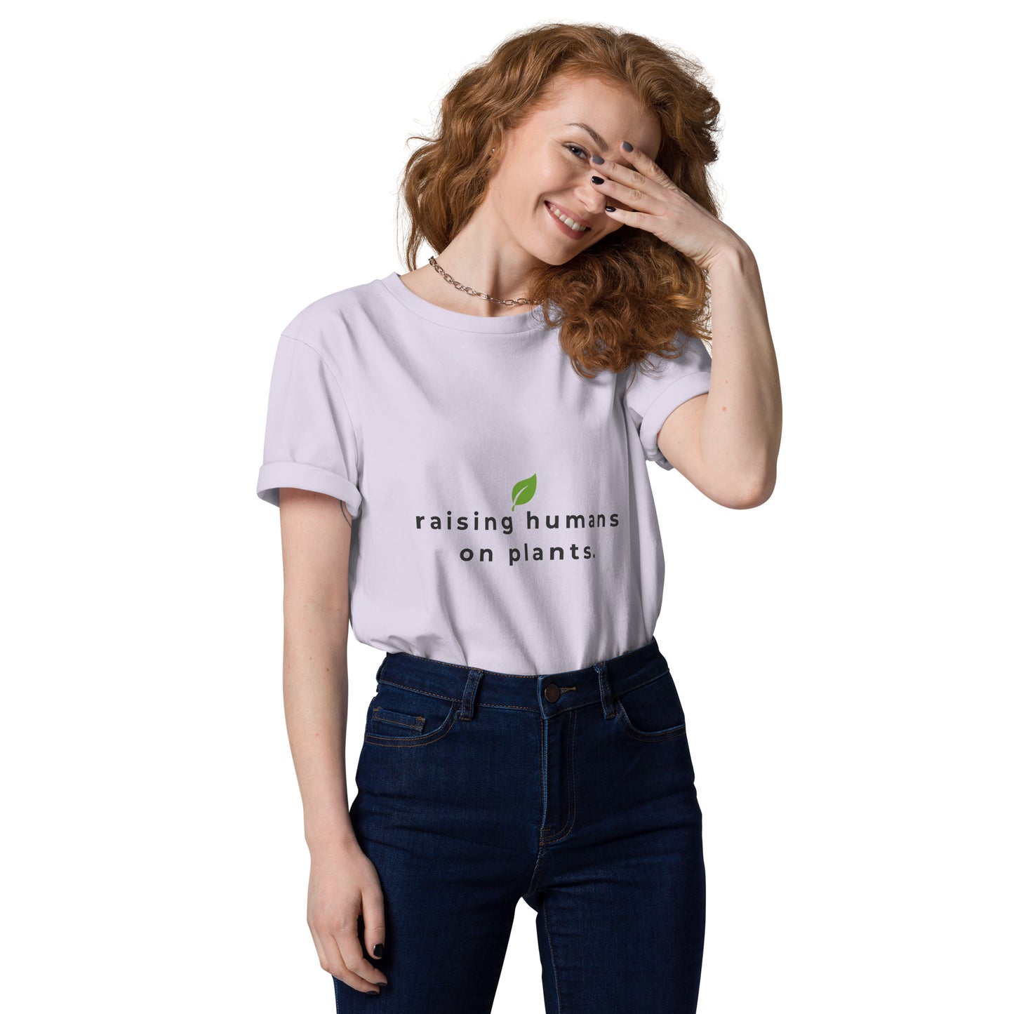 Smiling model wearing an eco-friendly lavender t-shirt. On the chest is printed the phrase "raising humans on plants." in charcoal grey with a small leaf centered above the text.