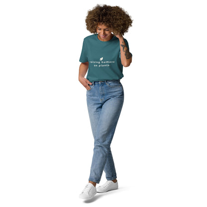 Model showing off a stargazer blue vegan t-shirt. The front graphic displays the motto "raising humans on plants." arranged in a clean, modern logo style.